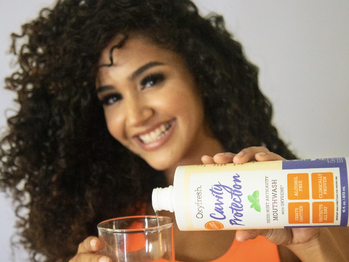 smiling-woman-pouring-oxyfresh-cavity-protection-sensitive-teeth-mouthwash-into-glass