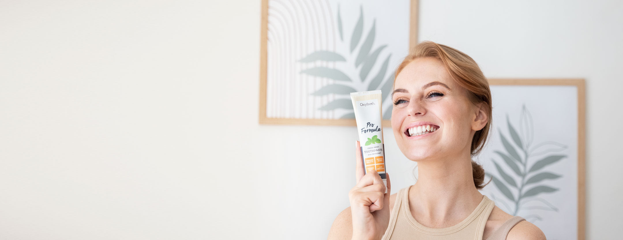 strawberry blond lady smiling brightly holding a tube of oxyfresh pro formula toothpaste which is gentle on her enamel to keep her teeth pearly white 